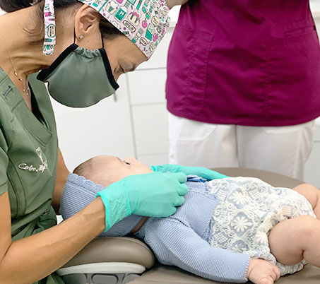 Odontopediatra revisando la boca de un bebé tumbado en el sillón durante su primera visita al dentista