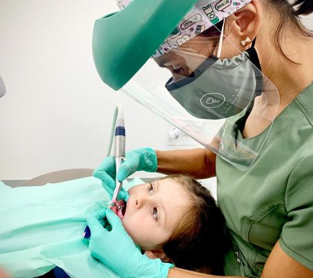 Odontóloga trabajando con contraángulo en la boca de una niña durante una valoración y limpieza dental infantil