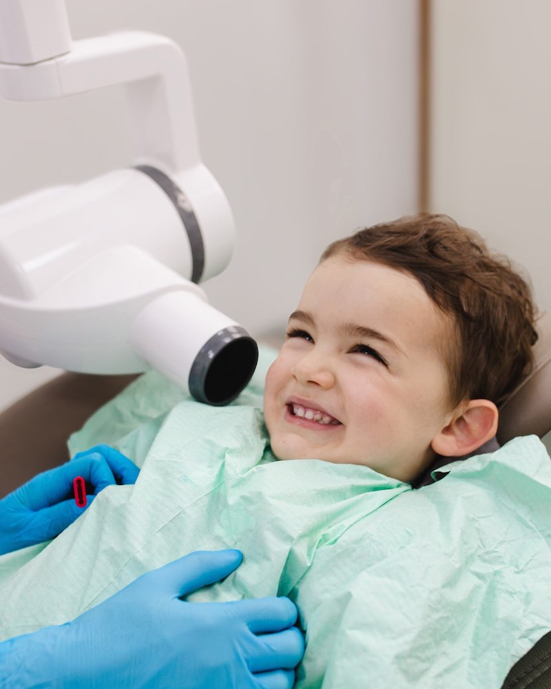 Niño sonriendo en el sillón junto al equipo de radiografía intraoral en la consulta de dentista infantil en Oviedo del Centro Odontológico Miguel González
